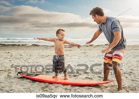 Young man teaching son to surf on beach View Large Photo Image Stock Photo - Young man teaching son to surf on beach. Fotosearch