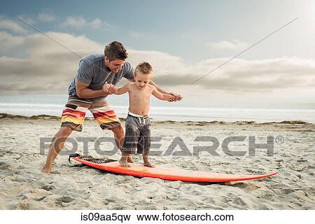 Stock Photo - Young man teaching son to surf on beach. Fotosearch