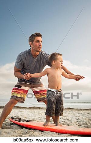 Stock Photo - Young man teaching son to surf on beach. Fotosearch