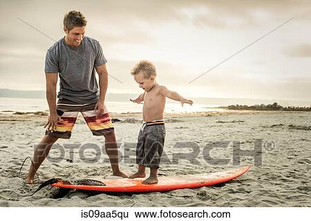 Young man teaching son to surf on beach View Large Photo Image Stock Photograph - Young man teaching son to surf on beach. Fotosearch
