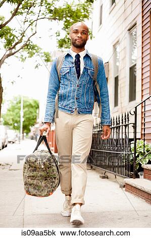 Stock Image - Young man walking down street with holdall. Fotosearch