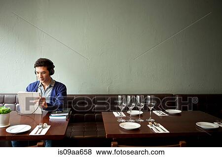 Stock Photo - Young man wearing headphones in restaurant. Fotosearch