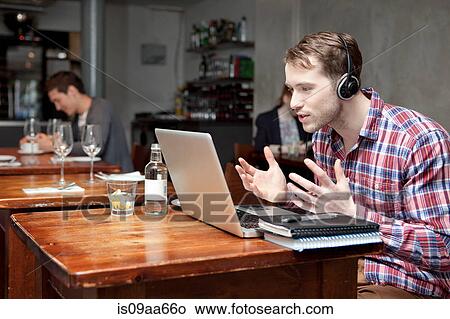 Young man wearing headphones using laptop in cafe View Large Photo Image Picture - Young man wearing headphones using laptop in cafe. Fotosearch