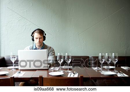 Stock Photo - Young man wearing headphones using laptop in restaurant. Fotosearch