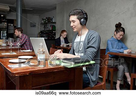 Young man wearing headphones using laptop in cafe View Large Photo Image Stock Photography - Young man wearing headphones using laptop in cafe. Fotosearch