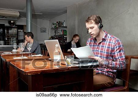 Stock Photography - Young man wearing headphones with laptop in cafe. Fotosearch