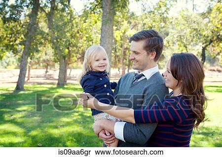 Stock Photography - Young parents in park holding female toddler. Fotosearch