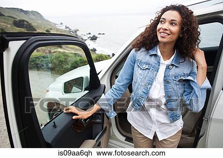 Stock Image - Young woman getting out of car at coast. Fotosearch