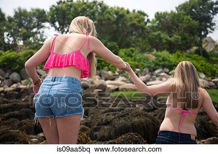 Stock Photography - Young woman holding hands with friend on beach, rear view. Fotosearch