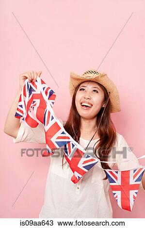Stock Image - Young woman holding Union flag bunting, smiling. Fotosearch