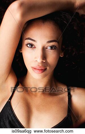 Stock Image - Young woman in against black background, portrait. Fotosearch