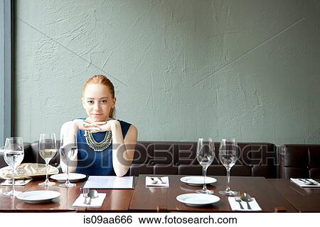 Stock Photograph - Young woman in restaurant, hands on chin. Fotosearch