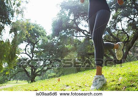 Stock Photograph - Young woman jogging through park, low section. Fotosearch