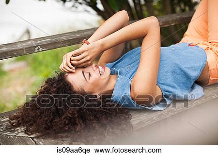 Stock Image - Young woman lying on picnic table, smiling. Fotosearch