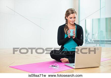 Stock Photo - Young woman on yoga mat with mug of tea. Fotosearch