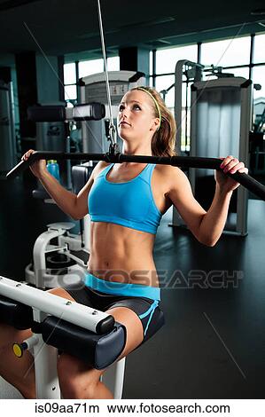 Picture - Young woman pulling weights in gym. Fotosearch