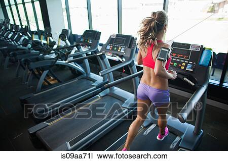 Stock Image - Young woman running on treadmill in gym. Fotosearch