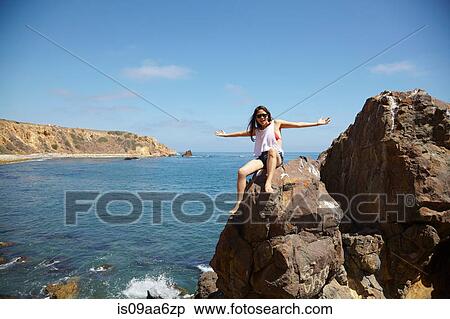 Stock Photography - Young woman sitting on rocks, Palos Verdes, California, USA. Fotosearch