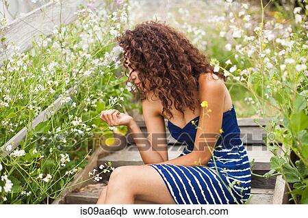 Young woman sitting on wooden steps looking at flower View Large Photo Image Stock Image - Young woman sitting on wooden steps looking at flower. Fotosearch