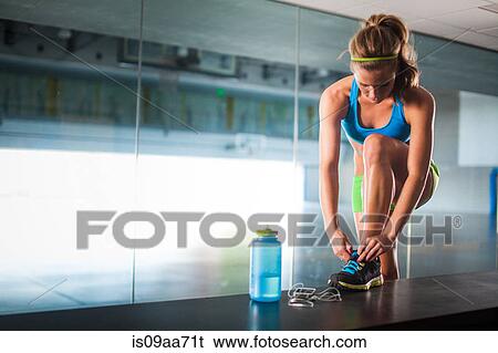 Stock Photograph - Young woman tying shoelace in gym. Fotosearch