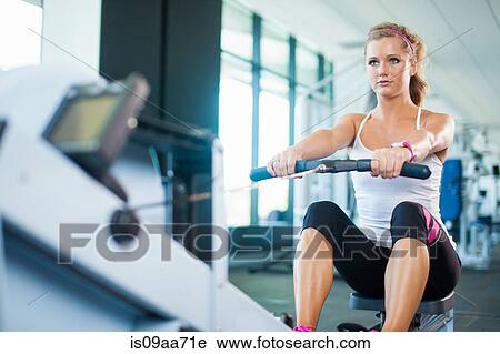 Stock Image - Young woman using rowing machine in gym. Fotosearch