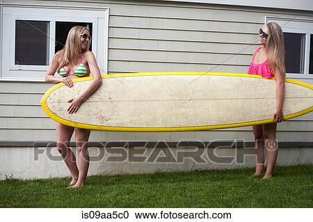 Stock Image - Young women carrying surfboard on grass. Fotosearch