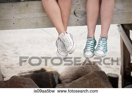 Young women sitting on pier on beach, low section View Large Photo Image Stock Photo - Young women sitting on pier on beach, low section. Fotosearch