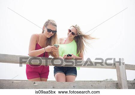 Young women using mobile phones on pier View Large Photo Image Stock Photo - Young women using mobile phones on pier. Fotosearch