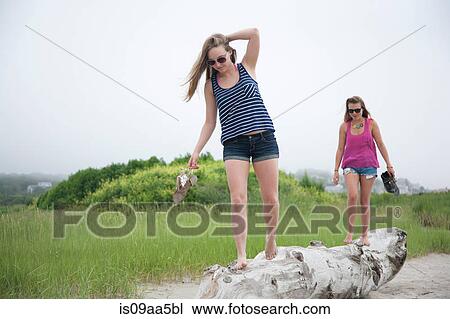 Stock Image - Young women walking along log on beach. Fotosearch