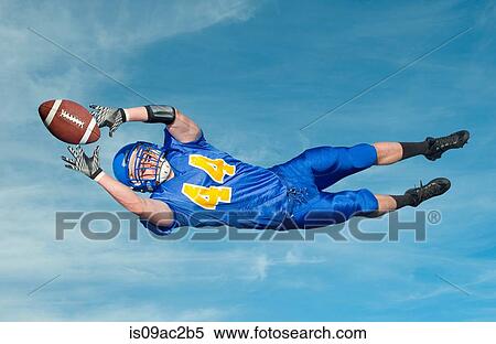 American footballer catching ball against blue sky View Large Photo Image Stock Photography - American footballer catching ball against blue sky. Fotosearch