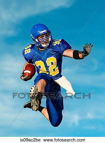 Stock Image - American footballer with ball against blue sky. Fotosearch