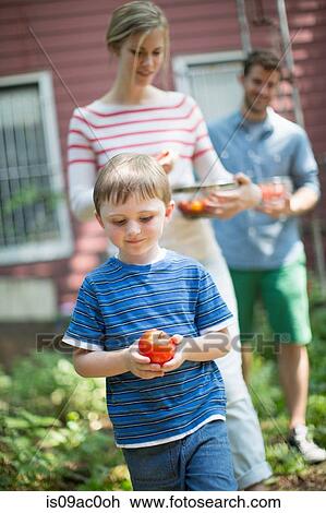 Stock Image - Boy holding apple with parents in background. Fotosearch