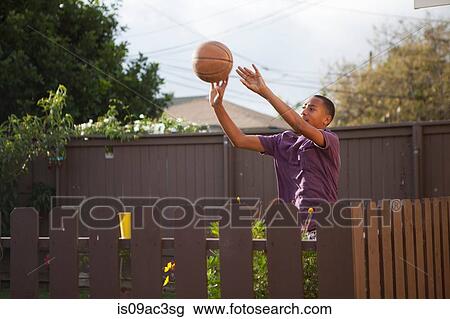 Stock Image - Boy throwing basketball near fence. Fotosearch