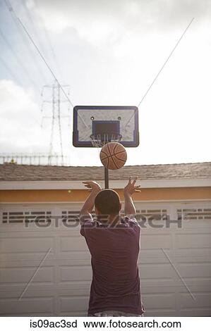 Stock Image - Boy throwing basketball towards hoop. Fotosearch