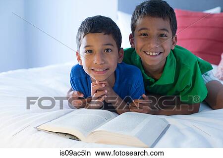 Picture - Brothers looking up from book on bed. Fotosearch