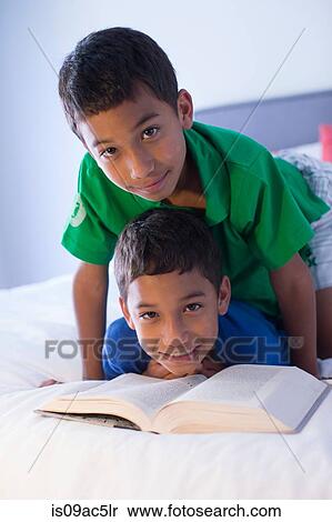 Brothers looking up from book on bed View Large Photo Image Stock Photography - Brothers looking up from book on bed. Fotosearch