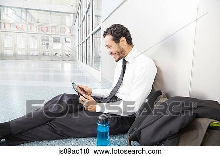 Stock Image - Businessman sitting on floor using digital tablet. Fotosearch