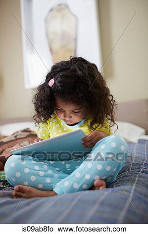 Child sitting on bed using digital tablet View Large Photo Image Picture - Child sitting on bed using digital tablet. Fotosearch