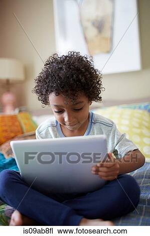 Stock Image - Child sitting on bed using digital tablet. Fotosearch
