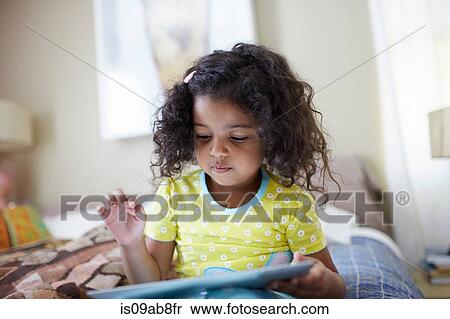 Stock Photography - Child sitting on bed using digital tablet. Fotosearch