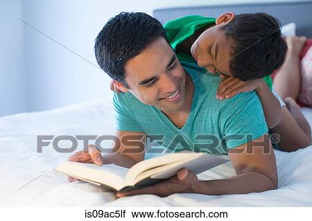 Stock Image - Father and son reading on bed. Fotosearch