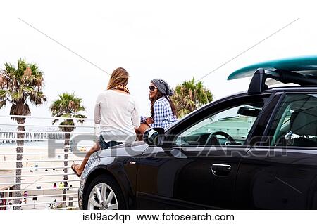 Picture - Female friends sitting on car, Hermosa Beach, California, USA. Fotosearch