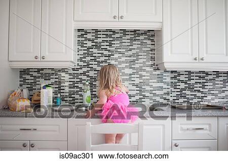 Stock Image - Girl standing on chair at kitchen counter. Fotosearch