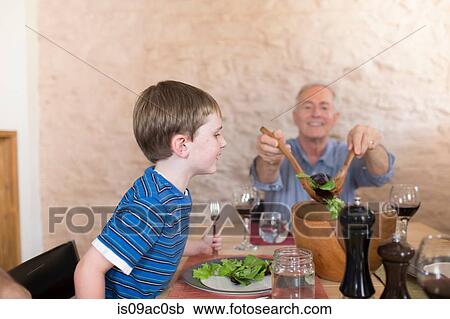 Stock Image - Grandfather and grandson at dinner table. Fotosearch