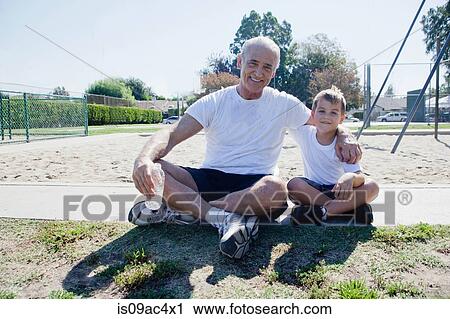 Stock Image - Grandfather and grandson sitting on sports field. Fotosearch