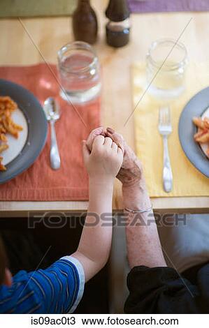 Stock Image - Grandmother and grandson holding hands at dinner table. Fotosearch