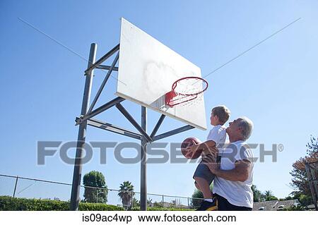 Stock Photography - Man lifting grandson to basketball hoop. Fotosearch