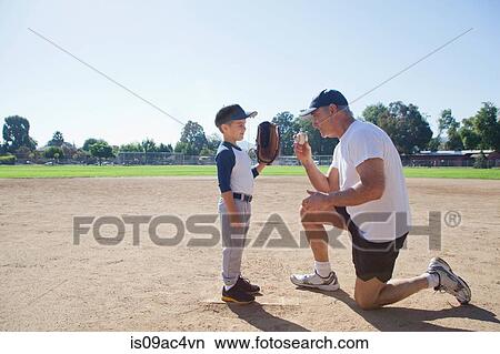 Picture - Man talking to grandson on baseball field. Fotosearch