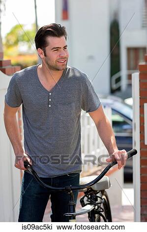 Stock Image - Man with bicycle standing on sidewalk. Fotosearch