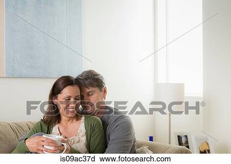 Stock Image - Mature couple sitting on sofa, woman with coffee. Fotosearch